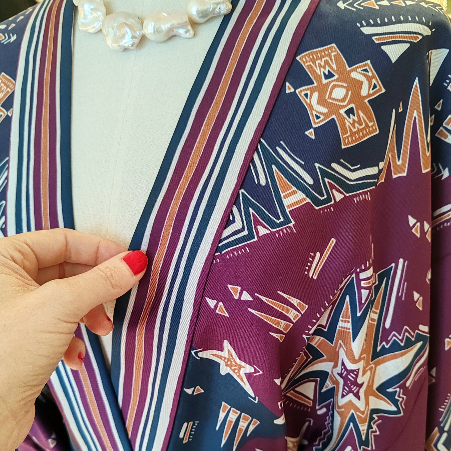 mano con smalto rosso che tiene il bordo di una giacca kimono in seta stampata blu e bordeaux