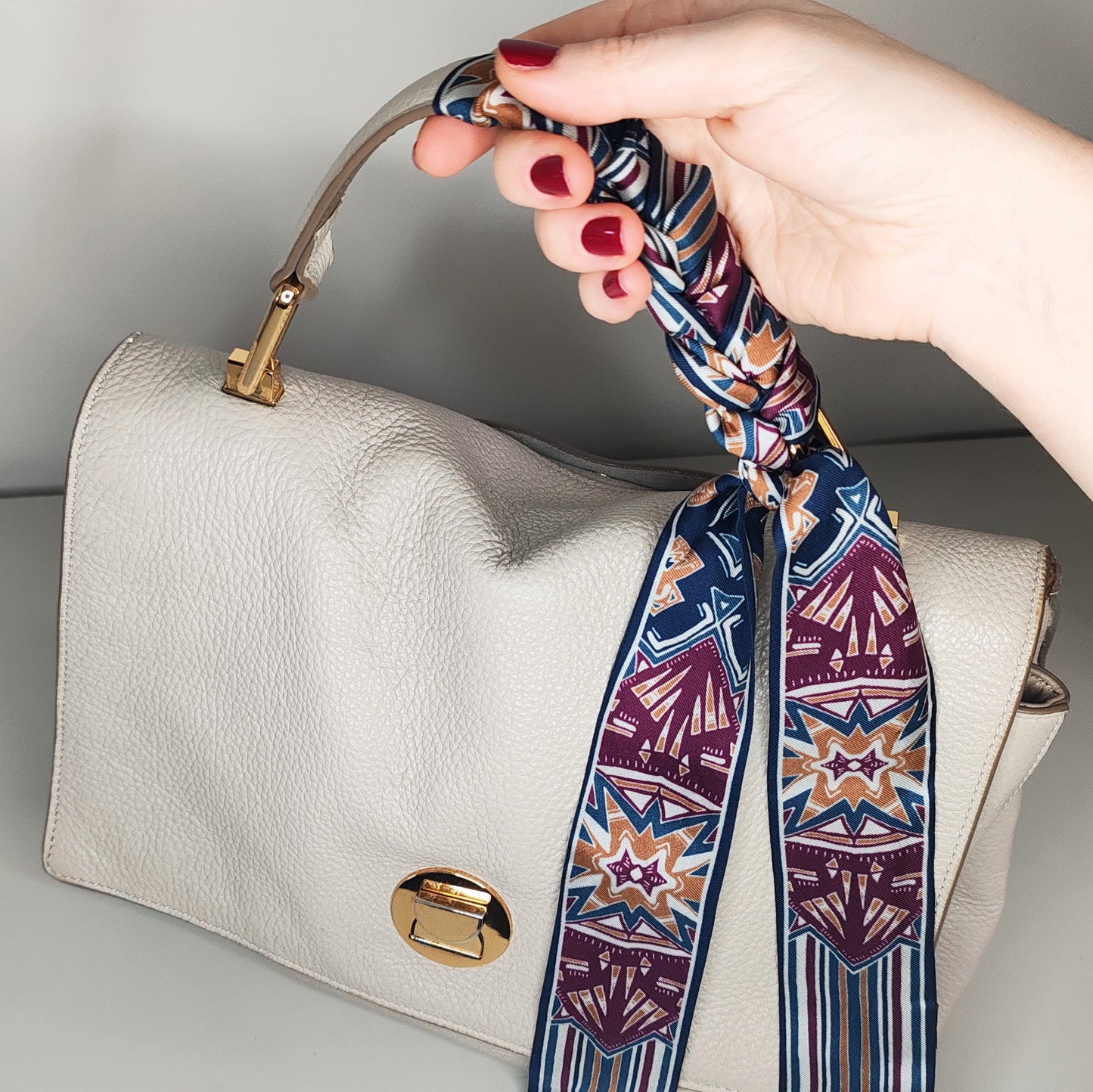 Fusciacca stampata in seta colore bordeaux avvolta al manico di una borsa avorio con mano modella smalto rosso