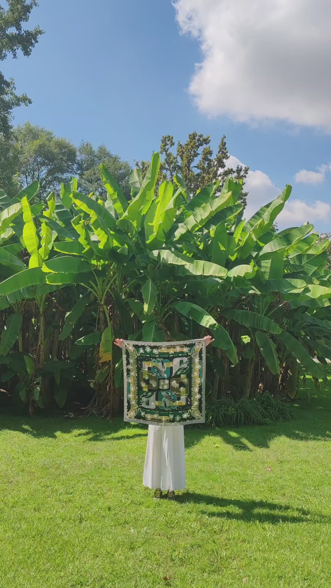 Carica il video: foulard carré 90x90 in seta naturale stampata con motivi disegnati a mano firmato Mon Lien dai torni verdi e immerso nella natura di un parco con palme sotto il sole con una modella che lo mostra in movimento